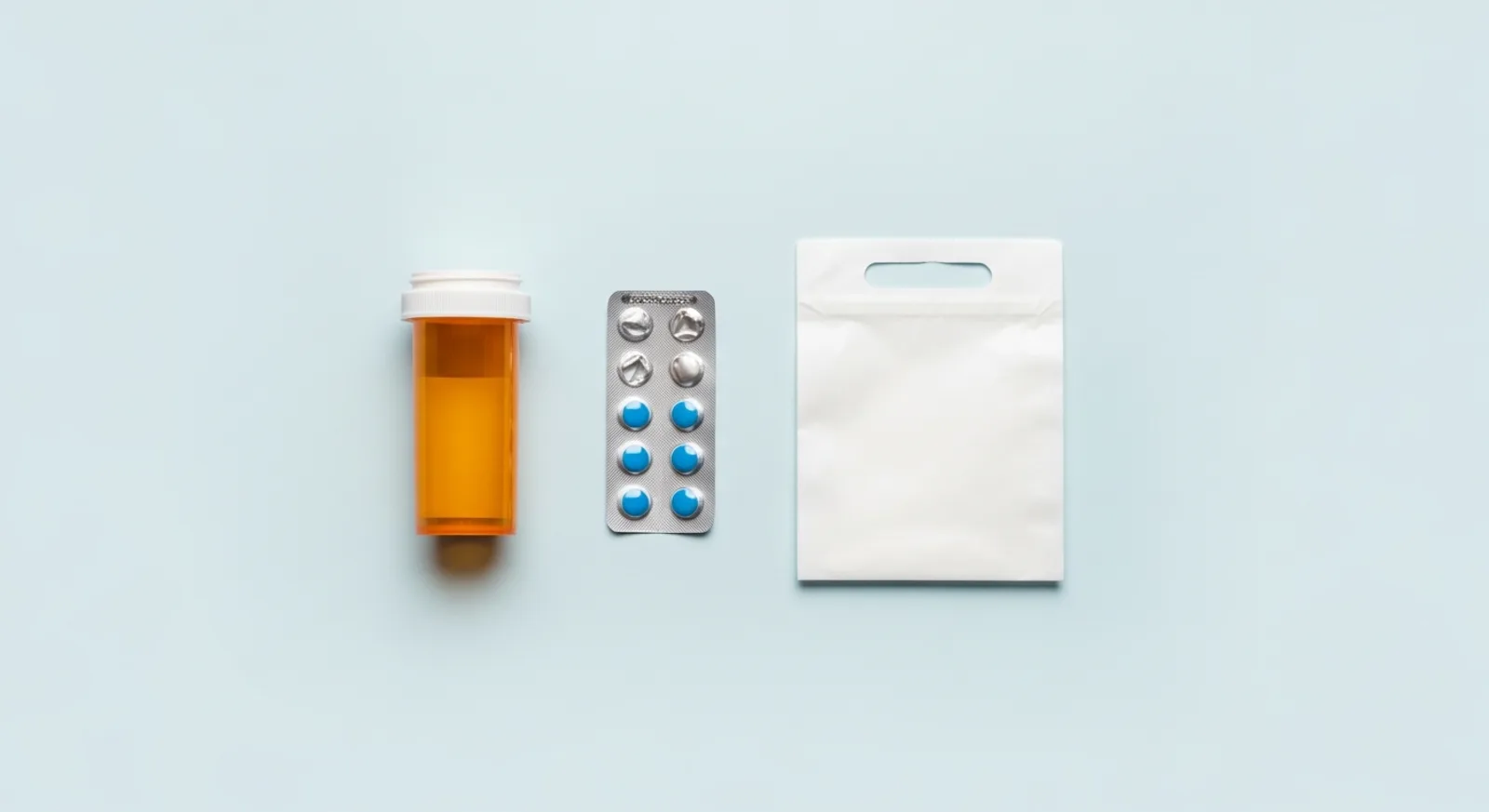 Prescription bottle, blister pack of tablets, and folded pharmacy bag on a light blue background