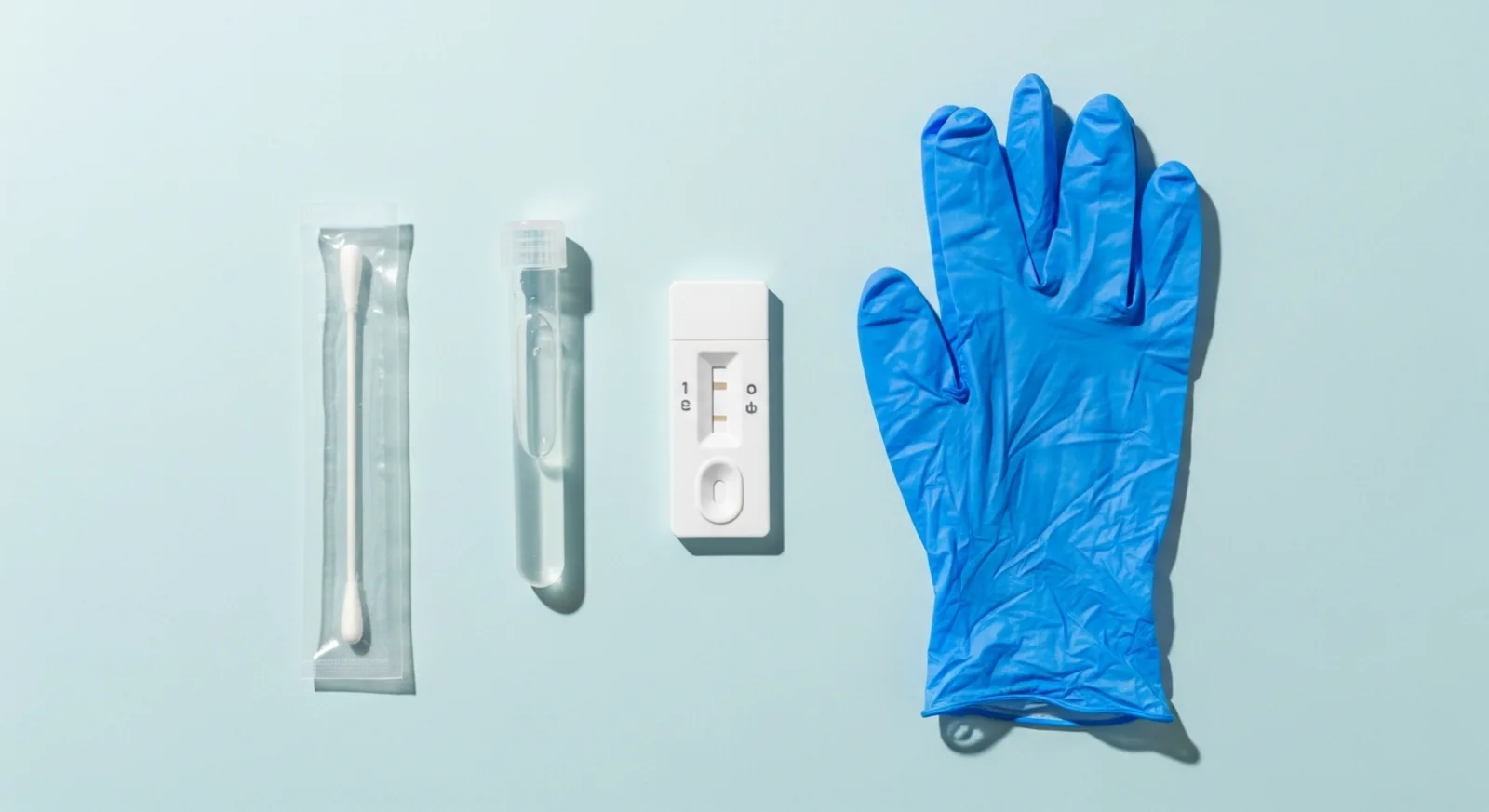 Sterile swab, test tube, rapid test cassette, and gloves arranged on a light blue background