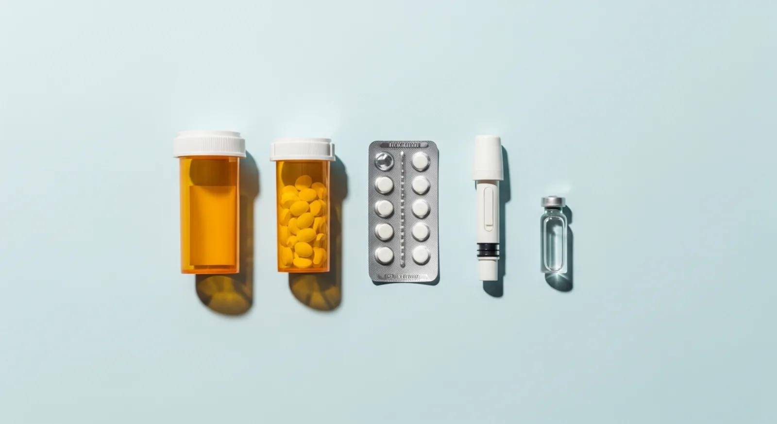 Specialty medication bottles, blister pack, and autoinjector pen arranged on a light blue background